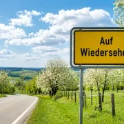 Eine Landstrasse  am Mittah mit einem Schild Auf Wiedersehen am Ortsausgang. Das Bild steht für troestliches Abschiedsdesign,