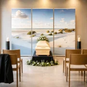 Dreiteiliges Roll-Up Display mit Nordseedünen-Motiv hinter einem hellen Holzsarg in einer modernen deutschen Trauerhalle mit zwei Kerzenleuchten, dezentem Blumenschmuck und Reihen aus Holzstühlen.