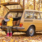 Ein Vater hilft seinem Sohn mit roten Gummistiefeln beim Einsteigen in einen historischen VW 412 Variant; der jüngere Bruder steht neben ihnen.