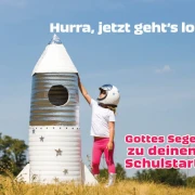 Kleines Mädchen als Astronautin auf einem Feld neben einer Papp-Rakete – Symbol für Aufbruch und Mut zum Schulanfang.