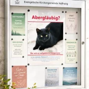 Moderner Gemeindeschaukasten mit dem christlichen Poster „Abergläubig?“ von Edition Katzenstein, umgeben von stilvoll gestalteten Gemeindeinformationen und Veranstaltungshinweisen.