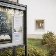 Betende Person vor einem Gemeindeschaukasten vor einer Kirche – Gebet als Grundlage einer segensreichen Schaukastengestaltung.