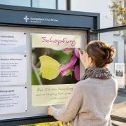 Ehrenamtliche Mitarbeiterin gestaltet einen Gemeindeschaukasten und hängt ein christliches Schaukastenposter in einer evangelischen Freikirche auf.