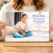 Frau hält das DIN-A4-Poster zur Jahreslosung 2027 mit Mädchen und Katze vor sich