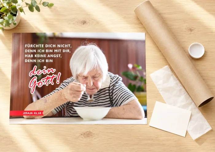 DIN-A3-Poster zur Jahreslosung 2027 mit Seniorin am Tisch neben stabiler Versandhülse