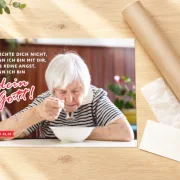 DIN-A3-Poster zur Jahreslosung 2027 mit Seniorin am Tisch neben stabiler Versandhülse