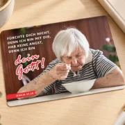 Produktfoto der Postkarte Jahreslosung 2027 mit älterer Frau allein am Tisch auf einem stilvollen Schreibtisch