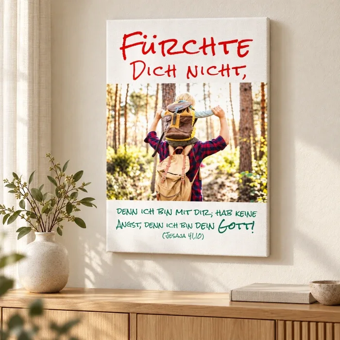 Leinwandbild zur Jahreslosung 2027 mit Vater-Sohn-Motiv über einer Holzkommode neben einer Vase im hellen Wohnzimmer.