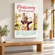 Leinwandbild Jahreslosung 2027 mit Vater und Sohn über einer Holzbank im hellen Kirchenfoyer, seitlich ein Holzkreuz.