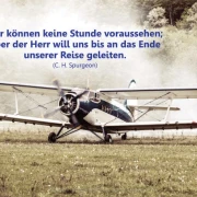 Ein altes Propellerflugzeug steht auf einer Graspiste, im Hintergrund Wald und Nebel. Darüber steht das Zitat von C. H. Spurgeon: „Wir können keine Stunde voraussehen; aber der Herr will uns bis an das Ende unserer Reise geleiten.“