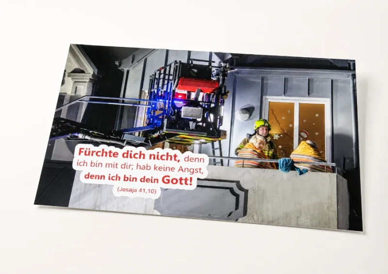 Freigestelltes DIN-A2-Poster zur Jahreslosung 2027 mit Feuerwehrmann und älterem Ehepaar
