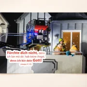 Poster Jahreslosung 2027 DIN A4 mit Feuerwehrmann und älterem Ehepaar bei einem Wohnungsbrand