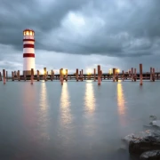 Leuchtturm vor dunklen Regenwolken, aufgenommen aus der Distanz.