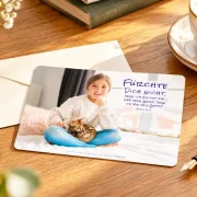 Postkarte zur Jahreslosung 2027 mit Mädchen und Katze neben Briefumschlag und Füller auf einem Schreibtisch
