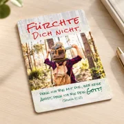 Eine Postkarte zur Jahreslosung 2027 liegt auf einem hellen Schreibtisch, danben sind Schreibgeräte zu sehen.