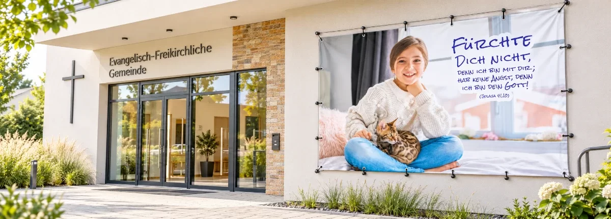 Banner zur Jahreslosung 2027 mit M&auml;dchen, Katze und Bibelvers aus Jesaja 41,10 an der Fassade eines modernen Gemeindehauses.